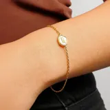 Pulsera dorada de cadena fina con dije redondo blanco con el signo de Acuario en dorado.