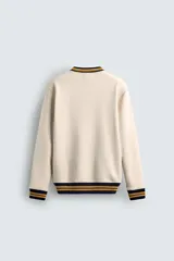 Sudadera color crema de corte regular fit, cuello redondo y manga larga. Presenta ribete a rayas en cuello, puños y bajo. Tiene un pequeño bordado de una flor en el pecho.