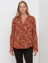 Blusa de manga larga color marrón terracota con estampado floral en tonos rojos, blancos y verdes. Presenta un escote en V con cuello mao y mangas que se pueden ajustar con presilla y botón.