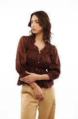 Blusa marrón de lino liviano con escote en V, abotonadura frontal y mangas 3/4 con puño. Diseño con frunces que generan un efecto entallado en la parte superior y amplio en el ruedo.