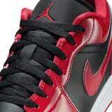 Zapatilla deportiva de corte bajo, color negro y rojo brillante (charol), con suela blanca y cordones negros. Presenta el logo Swoosh en negro y el logo de Air Jordan en el talón.