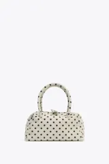 Bolso tipo bowling color crudo con estampado de lunares negros. Tiene doble asa de mano y correa bandolera extraíble. Incluye bolsillo interior con cremallera y cierre principal con doble cremallera.