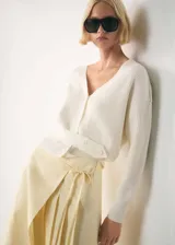 Cardigan de punto fino color crema, con cuello en V, cierre frontal con botones y mangas largas.