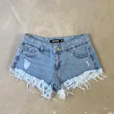 Short de jean celeste con efecto lavado, tiro alto, bolsillos delanteros y traseros, cierre con botón y cremallera. Detalle de flecos en el ruedo.
