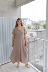 Vestido largo de manga corta, corte acampanado, color visón. Presenta un escote en V con detalle de terminación deshilachada o en picos desiguales en el ruedo.