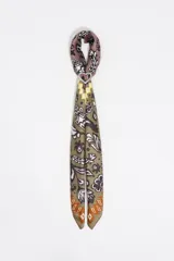 Pañuelo tipo twilly diseñado como charm para bolso, con estampado floral e ikat en tonos azul, verde, amarillo y naranja sobre fondo blanco. Incluye un anillo metálico plateado en forma de corazón que sujeta el pañuelo.