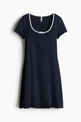 Vestido mini azul marino de manga corta en punto de algodón acanalado con pollera evasé. Modelo con cuerpo entallado y escote redondo amplio con ribete fino en color blanco y moña decorativa de satén. Ribete sobrehilado en mangas y bajo.