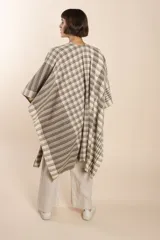 Ruana marrón con diseño a cuadros blancos, terminación envivada y flecos cortos.