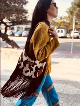 Cartera bandolera de cuero con estampado de vaca en blanco y marrón, base de cuero color chocolate y flecos largos color bordó.