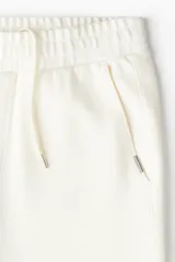 Pantalón jogger color crudo, de corte slim fit, confeccionado en sarga. Presenta cintura elástica con cordón ajustable, bolsillos laterales al bies y bolsillos traseros insertados.