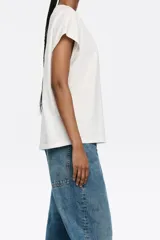 Camiseta blanca de algodón con corte recto, cuello redondo y mangas cortas tipo murciélago. Estampado frontal con el logo de la marca Bimba y Lola en color beige.