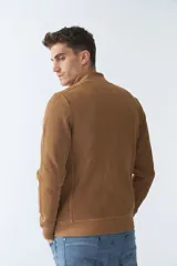 Campera marrón de algodón con cierre frontal, cuello alto, bolsillos laterales, puños y logo bordado en el pecho.