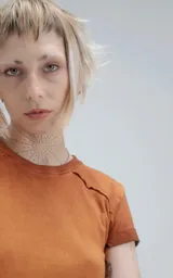 Remera de manga corta y cuello redondo, confeccionada en tejido ribb 100% algodón, de calce ajustado al cuerpo y largo a la cadera. El color es un marrón oscuro con efecto desgastado o teñido. Presenta costuras externas visibles en los hombros y laterales.