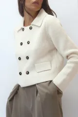 Chaqueta color crudo de tejido de punto con cuello solapa y manga larga. Tiene bolsillos de parche delanteros y cierre cruzado con doble botonadura.