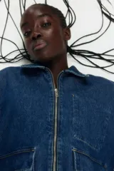 Campera de denim azul con cuello, cierre frontal y canesú en la espalda. Tiene puños abotonados, bolsillos delanteros con solapa y bolsillo interior de parche en el pecho.