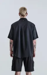 Camisa negra de manga corta con cuello clásico y cierre frontal con botones. Presenta una tira vertical cosida en el frente.