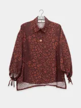 Camisa marrón con estampado animal print en tonos naranja, de corte holgado, cuello camisero, cierre frontal con botones y mangas largas con puños ajustables con lazos.