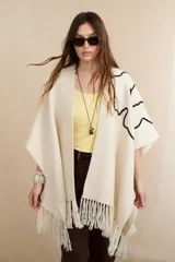 Ruana color crema con diseño bordado abstracto en negro y flecos en el ruedo.