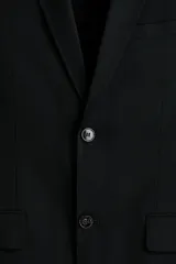 Blazer negro de tejido suave con solapas de muesca finas y ojal decorativo. Modelo de botonadura sencilla con un botón visible, bolsillo superior insertado, dos bolsillos delanteros con solapa y tres bolsillos interiores. Posee botones decorativos en los puños y abertura doble en la espalda. Corte ajustado.