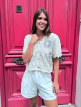 Blusa blanca de encaje con flores bordadas y botones al frente.