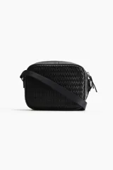 Bandolera negra con diseño trenzado, correa ajustable y cierre de cremallera.
