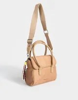 Cartera tipo city color beige, de tela deportiva, con doble asa corta, correa regulable desmontable, solapa con broche a presión y charm colgante.