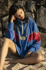 Hoodie azul de toalla con capucha, mangas largas y diseño color block con franja roja y ribete amarillo en el pecho. Logotipo bordado en el frente y bolsillos laterales.