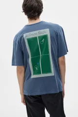 Remera azul con estampado en la espalda de una cancha de ping pong con raquetas y pelota, y la leyenda "Wellness Magic".