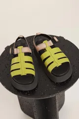 Sandalias Urban Haus con tiras anchas cruzadas color verde lima, ajuste con hebilla y plataforma plana color negro.