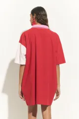 Túnica corta de mangas cortas con cuello camisero y cierre frontal con botones. Presenta un diseño bicolor con una franja diagonal en color beige.