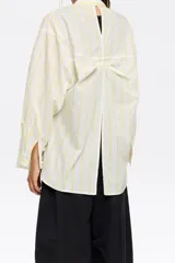 Camisa blanca con rayas verticales amarillas, de corte recto, manga larga con puños abotonados, cuello camisero y bolsillo de parche en el pecho.