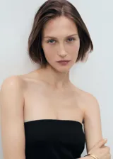 Vestido corto negro, sin mangas, con escote palabra de honor y falda evasé con tablas. Presenta cierre de cremallera en la parte posterior.