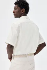 Camisa de manga corta color blanco, de corte recto, con cuello resort, cierre frontal con botones y bolsillo de parche en el pecho.