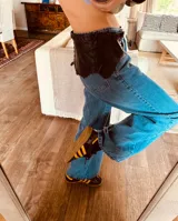 Cinturón ancho de cuero marrón oscuro con borde festoneado y cordones cruzados en la parte superior.