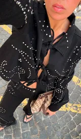 Chaqueta corta de denim negro con cuello clásico y cierre frontal con cordones. Decorada con tachas plateadas formando patrones ondulados.