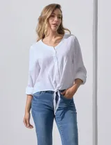 Blusa de algodón a rayas verticales finas en tonos blanco y lila, con escote en V, abertura frontal con botones y mangas largas regulables con presilla y botón. El ruedo termina anudado al frente.