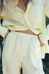 Pantalón tipo pijamero con tiro alto y cintura elástica, confeccionado en hilatura con algodón y lino. Presenta un estampado a rayas verticales en color amarillo y blanco, y detalle de botones decorativos en el delantero.