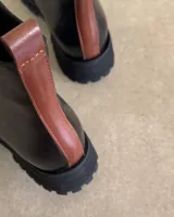 Botín de cuero vacuno negro con detalle de tira de cuero marrón en la parte trasera y suela track.