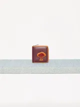 Billetera pequeña de cuero vacuno color bordó con cierre metálico y aplique de hongo. Interior con divisiones para tarjetas y forrería de tejido jacquard.