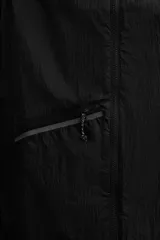 Chaleco negro de tejido técnico con estructura ripstop y ligero acolchado interior. Cuello alto ajustable con elástico, sisas amplias, bolsillos de seguridad con cremallera en pecho y cadera, acabados con cinta elástica, cierre frontal con cremallera y logo estampado en el bajo.