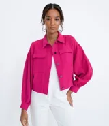 Campera color fucsia de crepe con cuello de camisa, manga abullonada, cierre frontal con botones y bolsillos frontales aplicados.