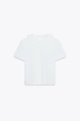 Camiseta blanca de manga corta con cuello bobo combinado a tono y acabados con fornituras a tono. Cierre en espalda con abertura y botón.