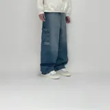 Pantalón jean azul de corte ultra baggy con bolsillos cargo y texto estampado en la pierna izquierda.