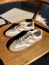 Championes de cuero color beige y blanco, con tachas plateadas en los laterales y suela de goma color caramelo.
