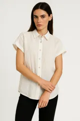 Camisa color beige de algodón, corte holgado, con cuello clásico y cierre frontal con botones.