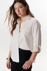 Camisa verde militar de manga larga con puños color crema, cuello clásico y cierre frontal con botones. Tiene un bolsillo en el pecho con bordado de una palmera color crema.