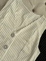 Conjunto blanco de chaleco y pantalón de vestir con finas rayas verticales. El chaleco es sin mangas, con cuello en V y cierre frontal con botones. El pantalón es de corte recto y tiro alto.