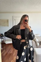 Chaqueta tipo bomber de cuero ovino marrón desgastado y gamuza color chocolate, con flecos largos en el canesú frontal y trasero. Presenta cuello solapa y cierre frontal con broches forrados.