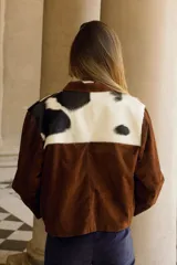 Chaqueta marrón de cuero vacuno con canesú delantero y trasero en cuero vacuno raza Holando (blanco con manchas negras), con cuello clásico, cierre frontal con botones y bolsillos laterales.