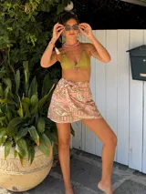 Falda pareo corta, color rosa pálido con estampado en tonos ocre/dorado. Presenta un diseño envolvente que se ajusta con un lazo lateral.